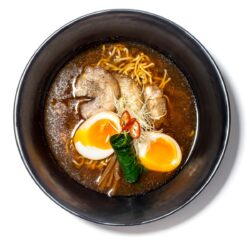 Ramen shoyu servido em taça preta com carne, ovo marinado e caldo de soja