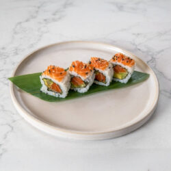 Uramaki Califórnia – Quatro peças de uramaki com salmão, abacate e pepino, cobertas com sementes de sésamo e servidas sobre folha de bambu.