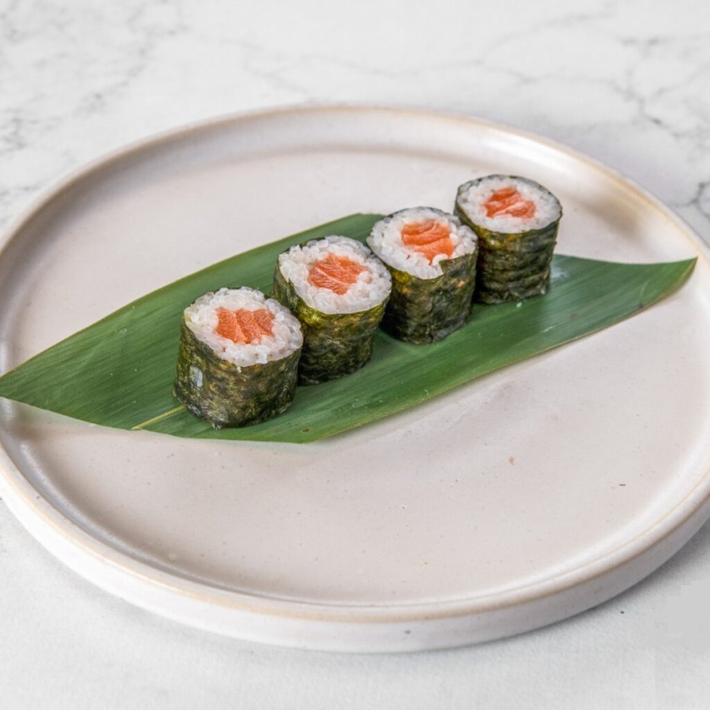 Hosomaki de salmão servido sobre folha verde em prato de cerâmica